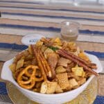 Fall Chex Mix Recipes 7 Flat lay of a sweet and salty fall Chex Mix recipe featuring golden Corn Chex, Cheerios, Wheat Chex, pretzels, mini saltine crackers, and cashews, all coated in a cinnamon sugar glaze and spread evenly on a baking sheet with a rustic fall cloth beneath.